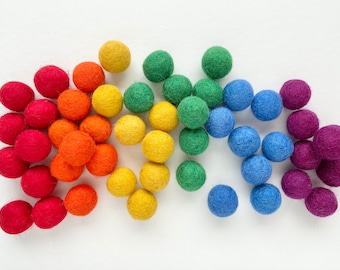 May include: A collection of colorful felt balls in a rainbow pattern. The balls are arranged in a semi-circle, with the red balls at the bottom and the purple balls at the top.