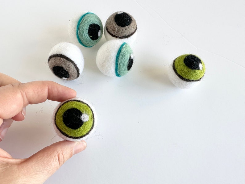 May include: Five felt eyeballs with different colored irises. The eyeballs are white with black pupils and green, brown, and blue irises.