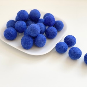 May include: A white plate filled with blue felt balls, with more blue felt balls scattered on a white surface.