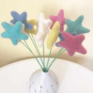 May include: A bouquet of felt star-shaped flowers in a white vase. The stars are in shades of blue, pink, yellow, and white.