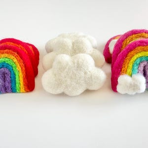 May include: Three felt rainbow arches and two felt clouds. The rainbows are layered with red, orange, yellow, green, blue, indigo, and violet. The clouds are white.