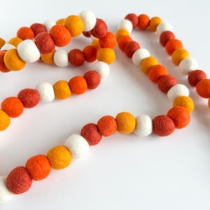 May include: A garland of felt balls in white, orange, and red. The balls are strung together on a white string.