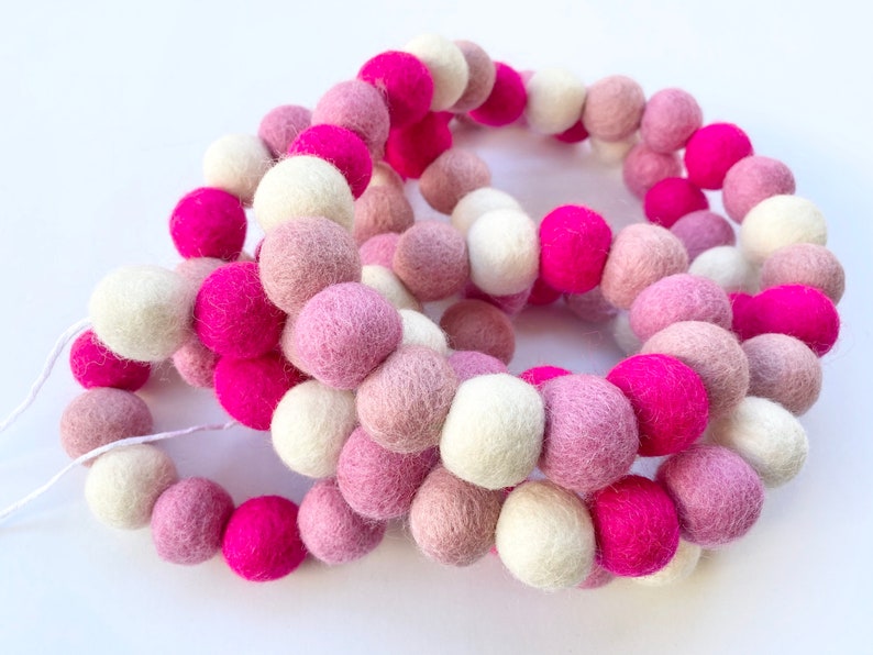 May include: A garland of felt balls in pink, white, and light pink colors. The balls are strung together on a white string.