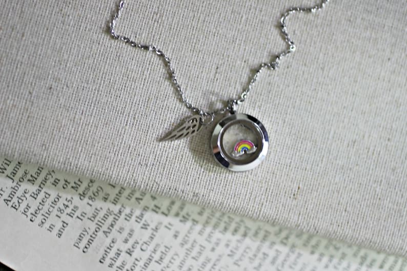 May include: A silver locket necklace with a rainbow charm inside. The locket is attached to a silver chain with a small silver wing charm.