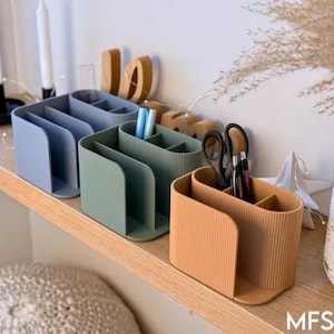 May include: Three oval-shaped desk organizers with a ribbed texture, arranged in a row. The organizers are colored in muted blue, sage green, and mustard yellow. Each unit features multiple compartments for storing stationery items like pens and scissors.