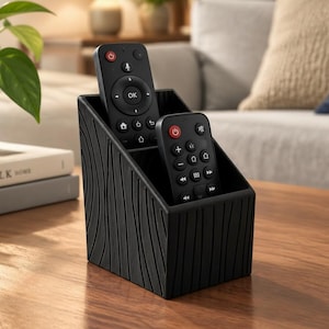 Peut inclure: Un organisateur de bureau noir avec un motif texturé de lignes verticales ondulées sur l'extérieur. Le récipient comporte deux compartiments distincts de hauteurs différentes, contenant deux télécommandes noires avec des boutons blancs.