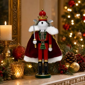 May include: A mouse nutcracker figurine wearing a red and gold crown, a red velvet cape with white faux fur trim, and a red uniform with green accents. The mouse holds a silver sword in one hand and stands on a circular green base.