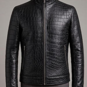 May include: A black leather jacket featuring a textured crocodile skin pattern, a high stand-up collar, and a full-length central metal zipper. The garment includes two vertical zippered pockets on the front and long sleeves with a fitted silhouette.