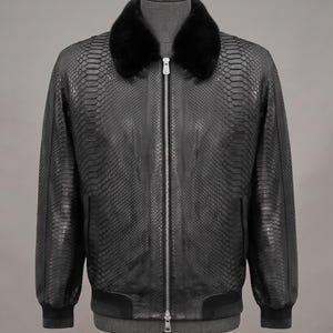 May include: A black jacket featuring a textured snakeskin pattern throughout the body, a solid black fur collar, and a central silver-toned metal zipper closure. The garment includes ribbed black cuffs and a ribbed hem at the bottom waistline.
