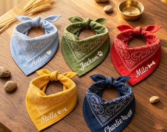 May include: Five pet bandanas in light blue, olive green, red, yellow, and navy blue, each featuring a white paisley pattern and a personalised name with a small icon: Arthur with a heart, Jackson with a paw, Milo with a bone, Stella with a fish skeleton, and Charlie with wings.
