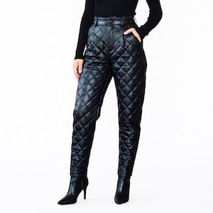 May include: High-waisted black trousers featuring a quilted diamond pattern throughout the legs. These pants include a button closure at the waistband, side pockets, and a tapered fit that extends down to the ankles, paired with black heeled boots.