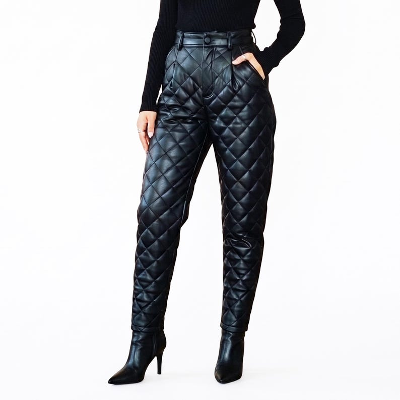 May include: High-waisted black trousers featuring a quilted diamond pattern throughout the legs. These pants include a button closure at the waistband, side pockets, and a tapered fit that extends down to the ankles, paired with black heeled boots.