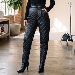 May include: Black high-waisted trousers featuring a quilted diamond pattern throughout the legs. The pants have a structured waistband with a button closure, side pockets, and a tapered fit, paired with black pointed-toe heeled ankle boots.