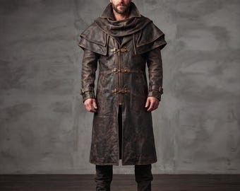 May include: A long, dark brown distressed leather coat featuring a high collar, a layered shoulder cape, and three ornate brass-toned metal toggle closures down the front. The coat includes long sleeves with adjustable buckled straps at the cuffs.