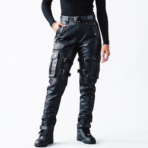 May include: Black leather cargo pants featuring a high-waisted belt, multiple side pockets with snap closures, and adjustable buckle straps on the thighs. The pants have a straight-leg fit with reinforced stitching details and matching black sneakers.