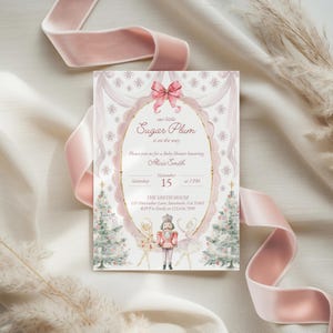 May include: A rectangular baby shower invitation card featuring a pink bow, a central oval frame, and Nutcracker-themed illustrations including two ballerinas and a nutcracker soldier. The text reads: our little Sugar Plum is on the way, Alicia Smith, November 15 at 2 PM, The Smith House, 125 Nutcracker Lane, Savannah, GA 31401, RSVP to Emily at 123.456.7890.