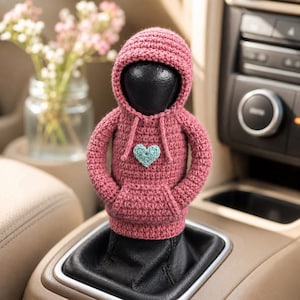 Può includere: Una copertura all'uncinetto color rosa polvere a forma di felpa con cappuccio per il pomello del cambio dell'auto. Il capo presenta un cappuccio con coulisse, maniche lunghe, una tasca a marsupio e un piccolo cuore all'uncinetto azzurro.