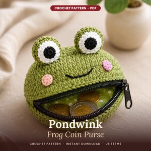 May include: A round, green crocheted coin purse shaped like a frog with white and black eyes, pink cheeks, and a black stitched smile. The purse features a black zipper opening revealing a green and white polka dot lining with gold coins inside.