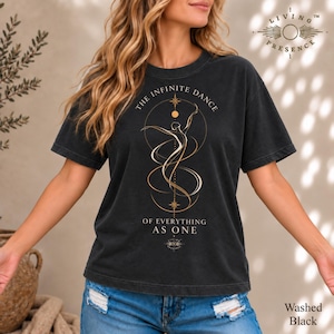 May include: A washed black short-sleeve t-shirt featuring a gold-toned graphic of a dancing figure surrounded by circular lines and stars. The text reads THE INFINITE DANCE OF EVERYTHING AS ONE, with a small logo at the bottom and LIVING PRESENCE above.