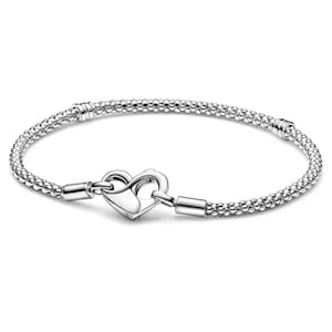 May include: A silver-toned bracelet featuring a textured, beaded chain design. The bracelet includes a heart-shaped clasp mechanism that connects the two ends of the chain, with smooth metal cylindrical accents positioned along the beaded band.