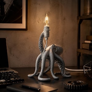 Puede incluir: Una lámpara de mesa con forma de pulpo gris y acabado texturizado. El pulpo tiene varios tentáculos que se extienden hacia afuera, con un tentáculo que se eleva para sostener una bombilla de filamento expuesto en un casquillo vertical.
