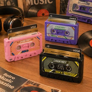 Op de afbeelding: Drie cassettevormige kaarthouders in roze, paars en zwart. Elke houder is voorzien van de tekst CASSTEET en SIDE B, met gleuven waarin meerdere creditcards zitten, waaronder Visa en American Express. Het ontwerp bootst vintage audiocassettes na.