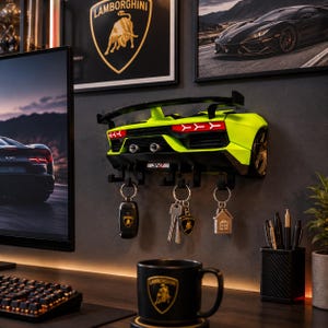 May include: A wall-mounted key holder shaped like the rear end of a lime green sports car with a black spoiler, dual exhaust pipes, and an SVJ emblem. The unit features five black hooks holding various metal keychains, including a car key fob.