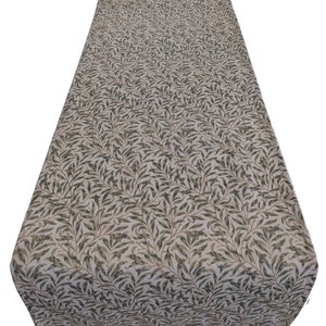 May include: A white tablecloth with a green and brown willow pattern. The pattern is a repeating design of leaves and branches.