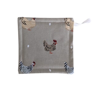 May include: A beige kitchen pot holder with a white loop handle. The pot holder features a repeating pattern of brown and white chickens and white eggs on a beige background.