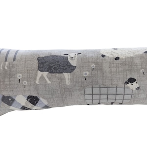 May include: A grey and white doorstop shaped like a cylinder with a sheep pattern. The sheep are black, white, and grey and are printed on a textured fabric.