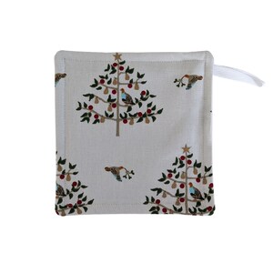May include: Square, cream-coloured pot holder featuring a repeating pattern of Christmas trees, birds, and berries. The trees are brown with green leaves, red berries, and gold star toppers. A white loop is attached to one corner.