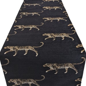 Può includere: Tovaglia da tavolo nera con un motivo ripetitivo di silhouette di leopardi dorati.