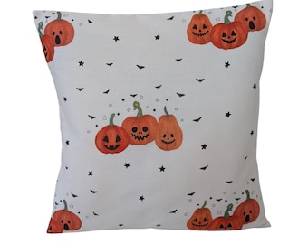 May include: Square decorative pillow with a white background featuring orange jack-o'-lanterns, black bats, and stars. The pumpkins have various carved faces. A festive Halloween-themed home decor item.
