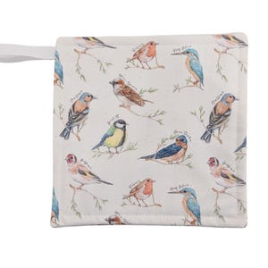 May include: A square, cream-coloured pot holder with a hanging loop, decorated with a pattern of various birds on branches. The design includes robins, kingfishers, and finches, with handwritten labels. The pot holder is made of quilted fabric.