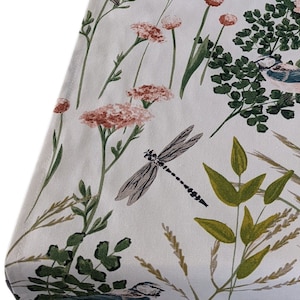 May include: A white fabric with a floral pattern featuring pink flowers, green leaves, and a dragonfly. The fabric has a subtle texture.