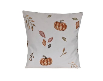 May include: Square decorative pillow with a cream background and a repeating pattern of watercolor pumpkins and autumn leaves in shades of brown, orange, and green. The pillow has a soft, inviting appearance.