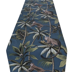 以下が含まれることがあります： 熱帯ジャングルをデザインした青いテーブルランナー。ヤシの木、緑豊かな葉、茶色の猿の模様。猿は様々なポーズで描かれており、バナナを持っているものもいます。ランナーは柔らかく、おそらく織られた素材で作られています。