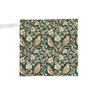 May include: A square, green fabric item featuring a repeating pattern of birds, flowers, and leaves. The birds are brown and beige, the flowers are cream-coloured, and the leaves are a muted green. A white fabric loop is attached to the side.
