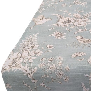 May include: A light blue tablecloth with a floral and bird pattern. The pattern features white flowers, brown leaves, and brown birds.