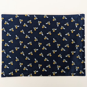May include: A navy blue placemat with a repeating pattern of yellow and black bees.