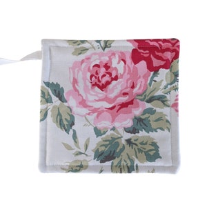 Puede incluir: Un agarrador de olla de algodón blanco con un patrón floral con rosas rosas y rojas y hojas verdes.