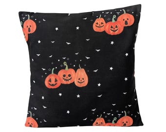 May include: Black decorative pillow with a Halloween theme. The pillow features orange pumpkins with carved faces, white stars, and bat silhouettes scattered across the surface. The pumpkins have various expressions.
