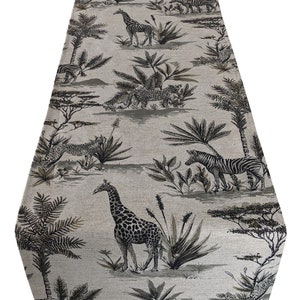 May include: A beige table runner with a black and white safari animal print. The print features giraffes, zebras, and leopards in a jungle setting.