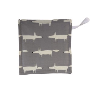 以下が含まれることがあります： グレーと白の鍋つかみで、グレーの背景に白いキツネが繰り返し描かれたパターンがあります。鍋つかみには白いループハンドルが付いています。