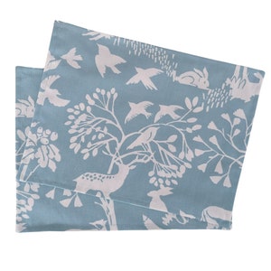 May include: A set of two blue placemats with a white woodland design featuring deer, birds, and trees.