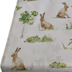 Può includere: Tessuto bianco con un motivo ripetuto di conigli marroni e fogliame verde. I conigli sono in varie pose, alcuni seduti, alcuni in piedi e alcuni che corrono. Il fogliame è in stile acquerello con sfumature di verde e marrone.