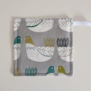 May include: A grey and white pot holder with a bird and leaf pattern. The pot holder has a white loop for hanging.
