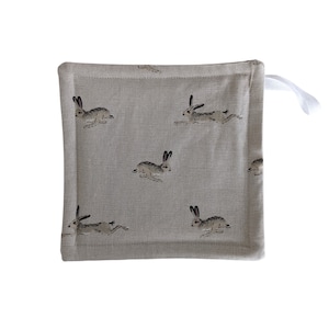 May include: Square, light gray pot holder with a repeating pattern of running hares in shades of gray and brown. A white loop is attached to one corner. The pot holder is made of a textured fabric.