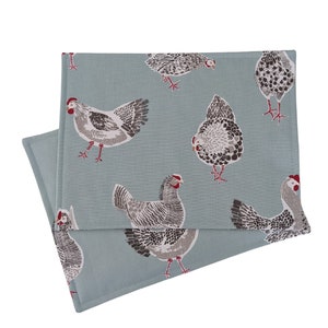 May include: A set of two blue placemats with a white and grey chicken pattern. The placemats are made of a soft, textured fabric.
