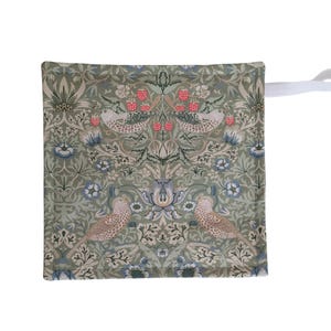 May include: A square, sage green oven glove with a white loop. The glove features a detailed pattern of birds, flowers, and berries in shades of green, blue, and pink. The design is symmetrical and ornate.